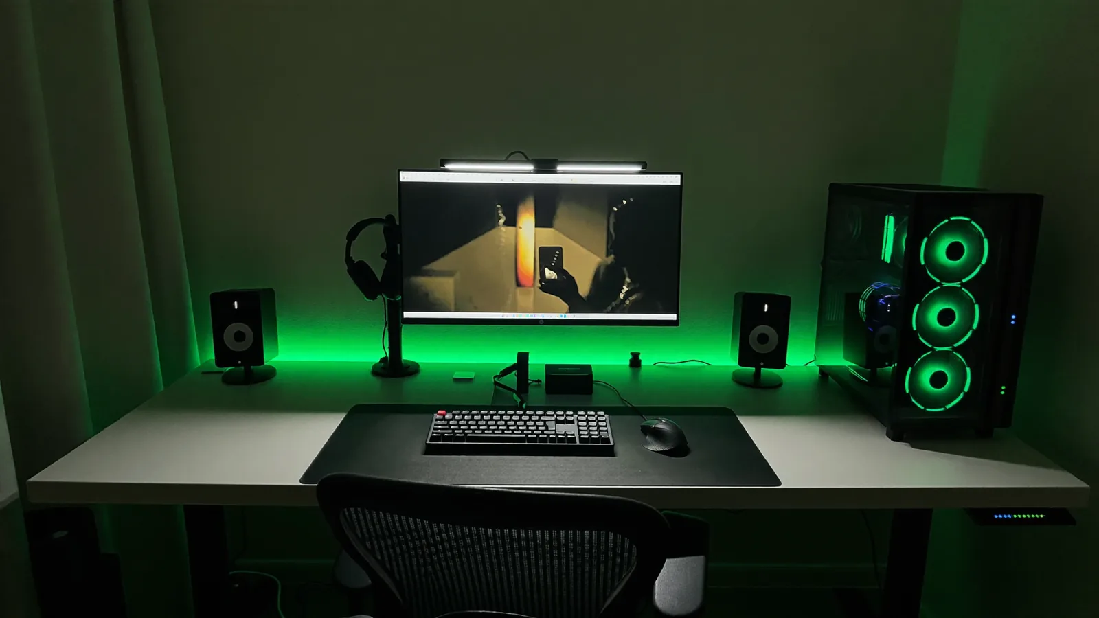 Setup de escritorio oscuro con monitor, teclado, parlantes y luces verdes